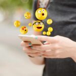 cellulare tenuto in mano da cui escono emoji