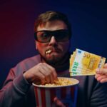 uomo che mangia popcorn al buio con una man oche offre soldi